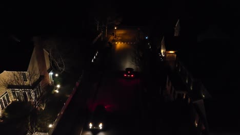 aerial tracking shot of two cars passing each other in dark neighborhood at night