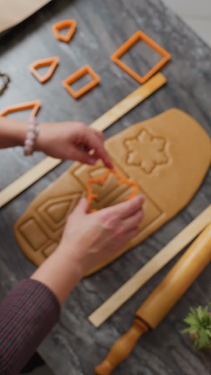 vista aérea de un panadero presionando un cortador de naranja sobre la masa enrollada, creando formas precisas, herramientas de horneado, rodillo y bandeja de madera con harina cerca