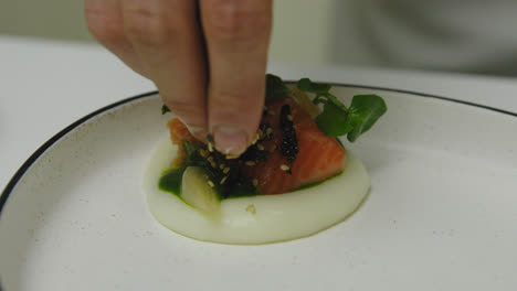 close up shot of starred chef adding sesame and seaweed on salmon meal