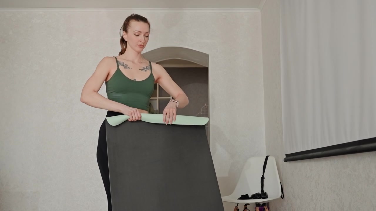 Donna con tappetino da yoga. Sistemare i tappetini per una sessione di yoga al chiuso. Preparare i tappetini da yoga per l'esercizio a casa. La donna organizza i suoi tappetini da yoga nel soggiorno per una sessione di pratica a casa.