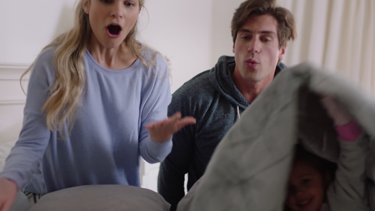 행복한 가족과 아이들이 침대에 뛰어들고 엄마와 아빠와 함께 놀고 주말 아침에 재미를 느끼고 흥분된 어린 아이들이 부모와 함께 집에서 게임을 즐기고 있습니다. 4k 영상