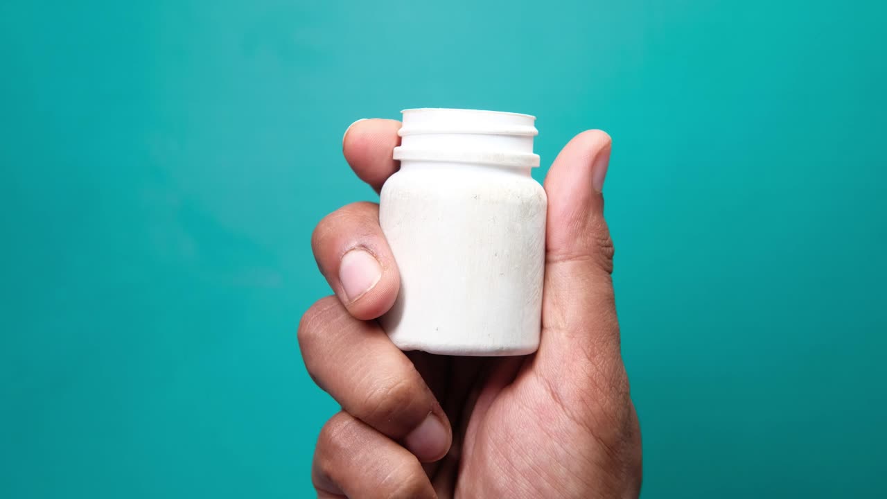 Mano sosteniendo un frasco de pastillas de plástico blanco