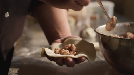 adding pork meat filling to dumplings, closeup on chef hands