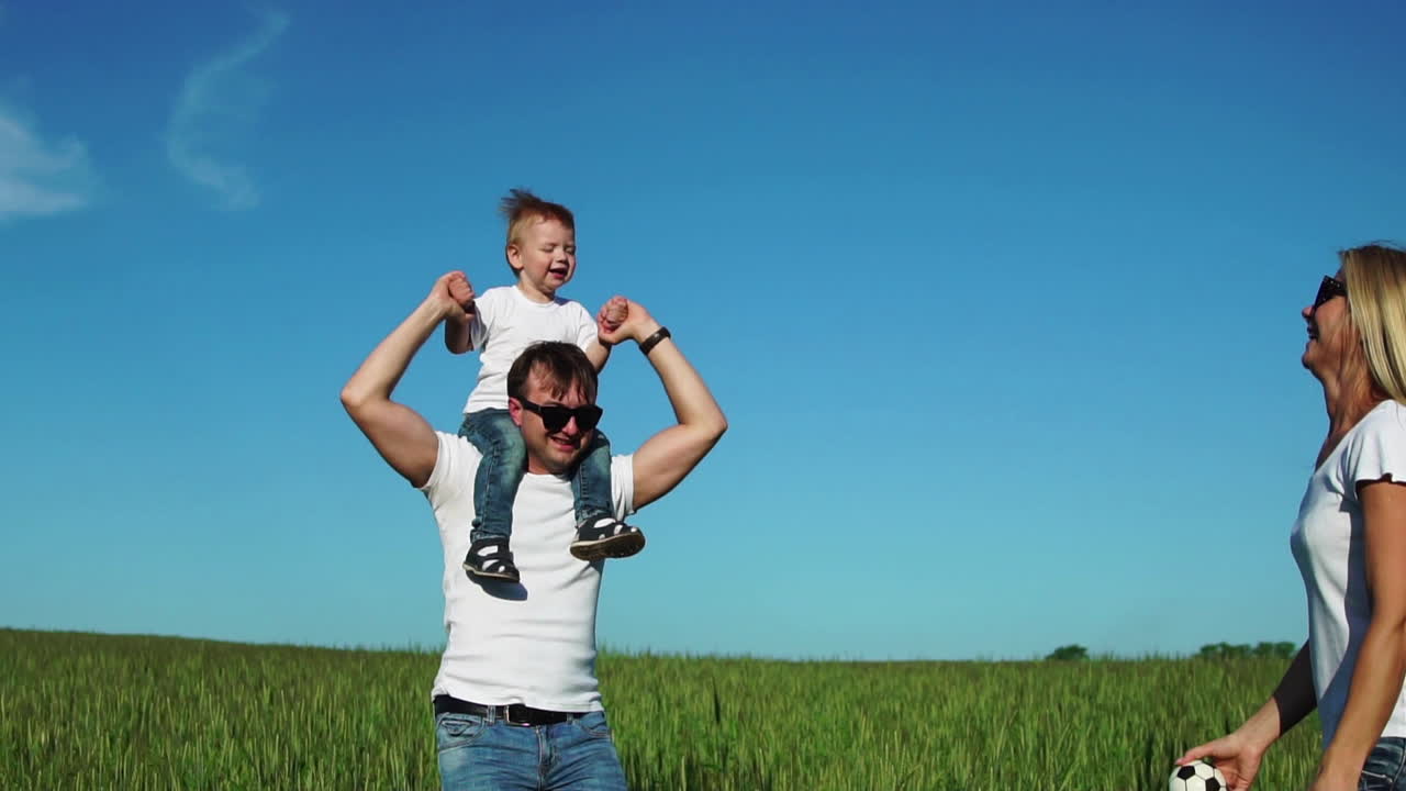 Happy family in the field on a Sunny day in the Park having fun and spending time together. The son sits on his father's shoulders
