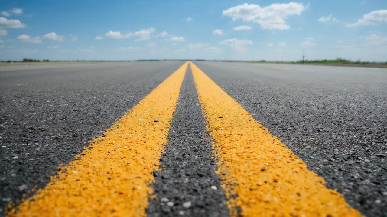 Starting camera filming paired yellow center lines on rural road, grass shoulders, sign, clouds