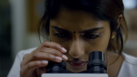 close-up of a woman looking through a microscope in a lab