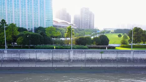 aerial shot of a man running in a park along a river with big buildings in the background in hangzhou, china