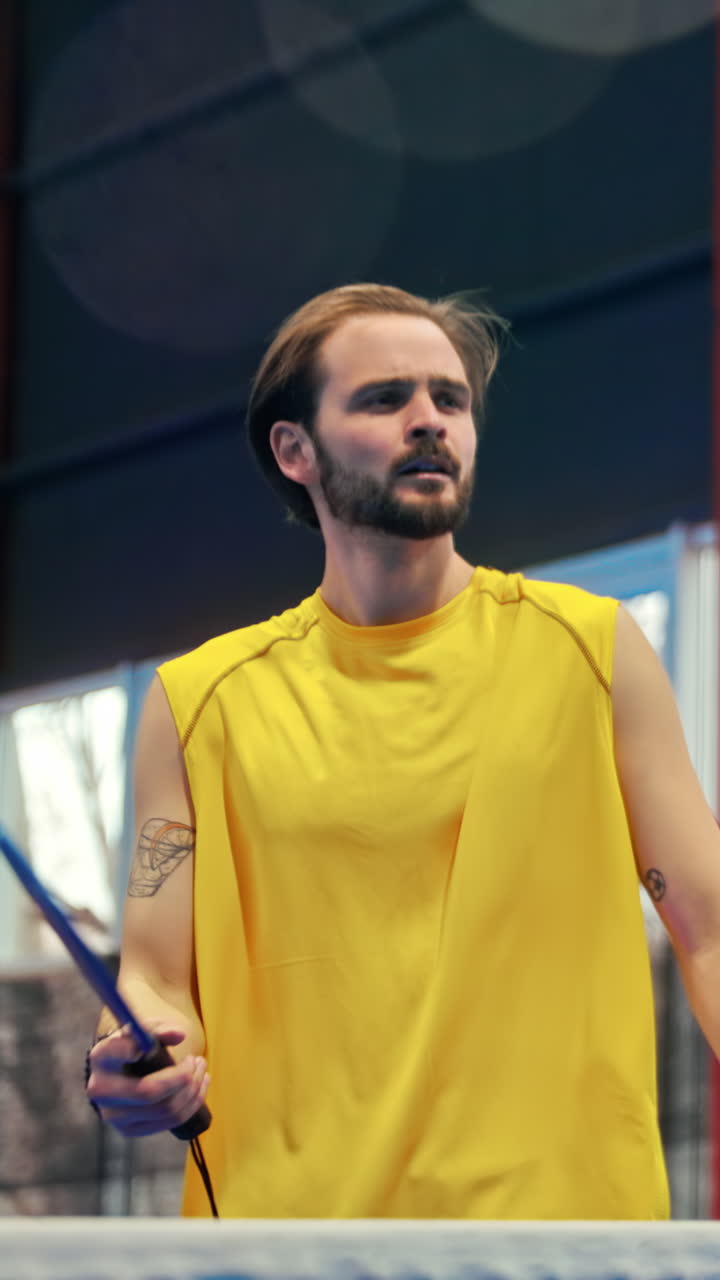 Man in yellow shirt playing pickleball on a blue, inside court. Vertical