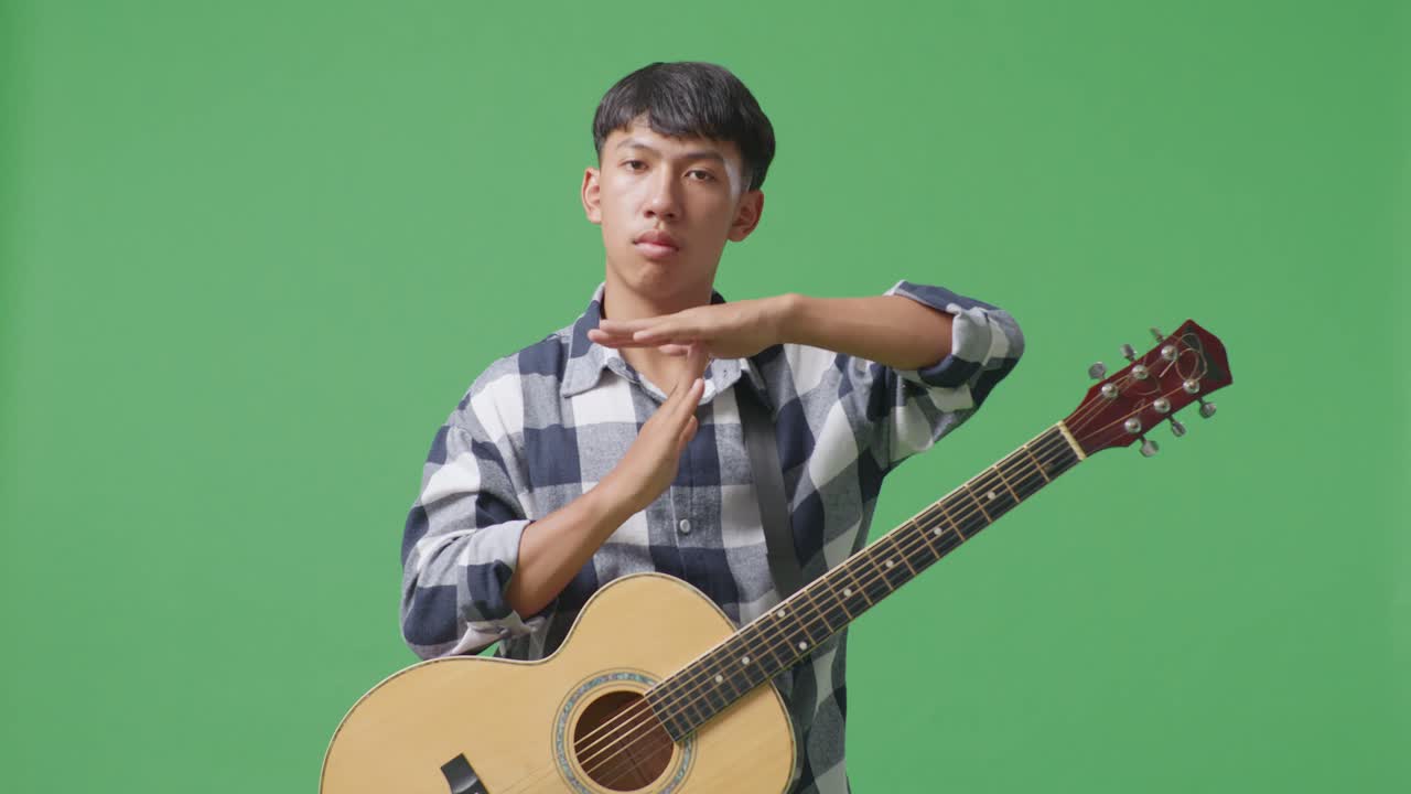 기타를 들고 있는 아시아인 십대가 녹색 화면 배경에 손을 고 타이밍 아웃을 하고 있다.