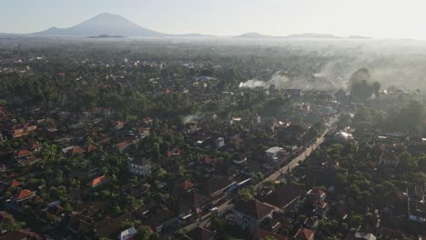 Establishing-scene-of-downtown-Ubud-in-early-morning-with-busy-traffic-and-fire-from-burning-trash-in-Bali,-Indonesia