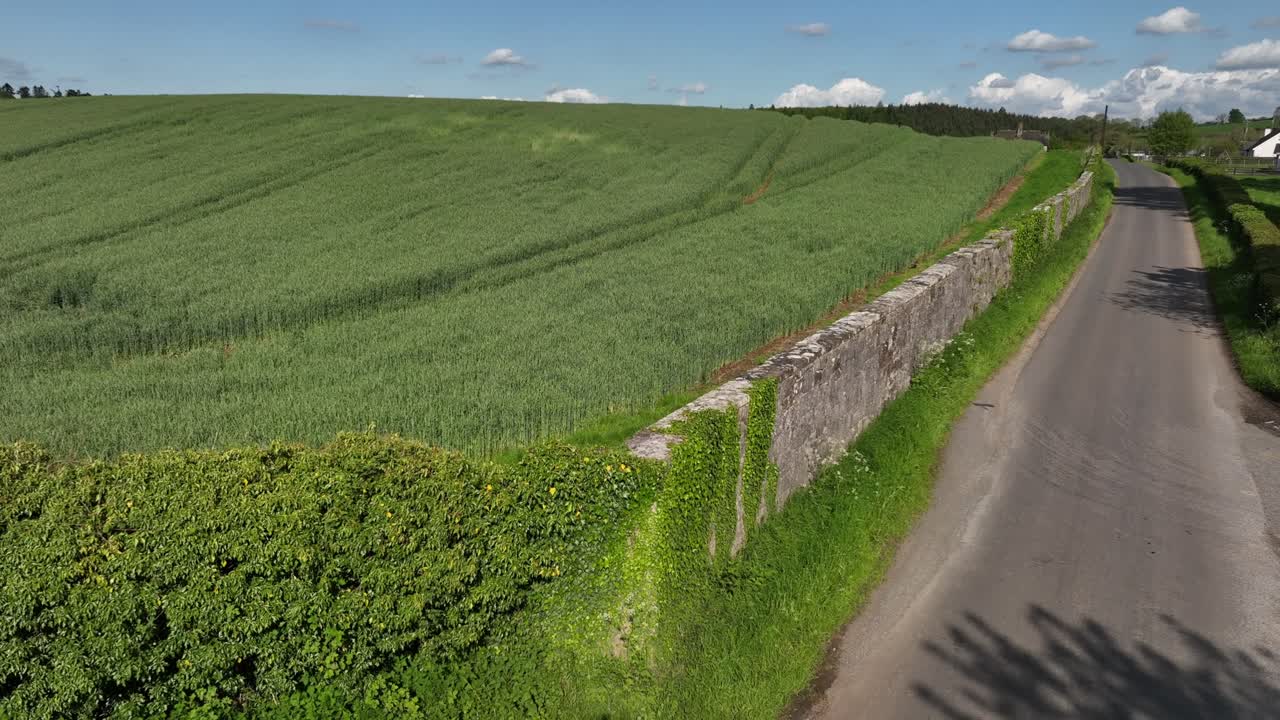 Caledon Border Wall, County Tyrone, Northern Ireland, May 2023. Drone slowly ascending over border wall, scenic road, lush farmlands and peaceful Irish countryside in summer.