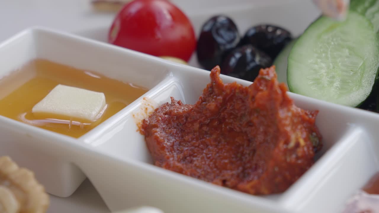 A close-up of a diverse breakfast spread featuring cheese, honey, olives, vegetables, and pastries