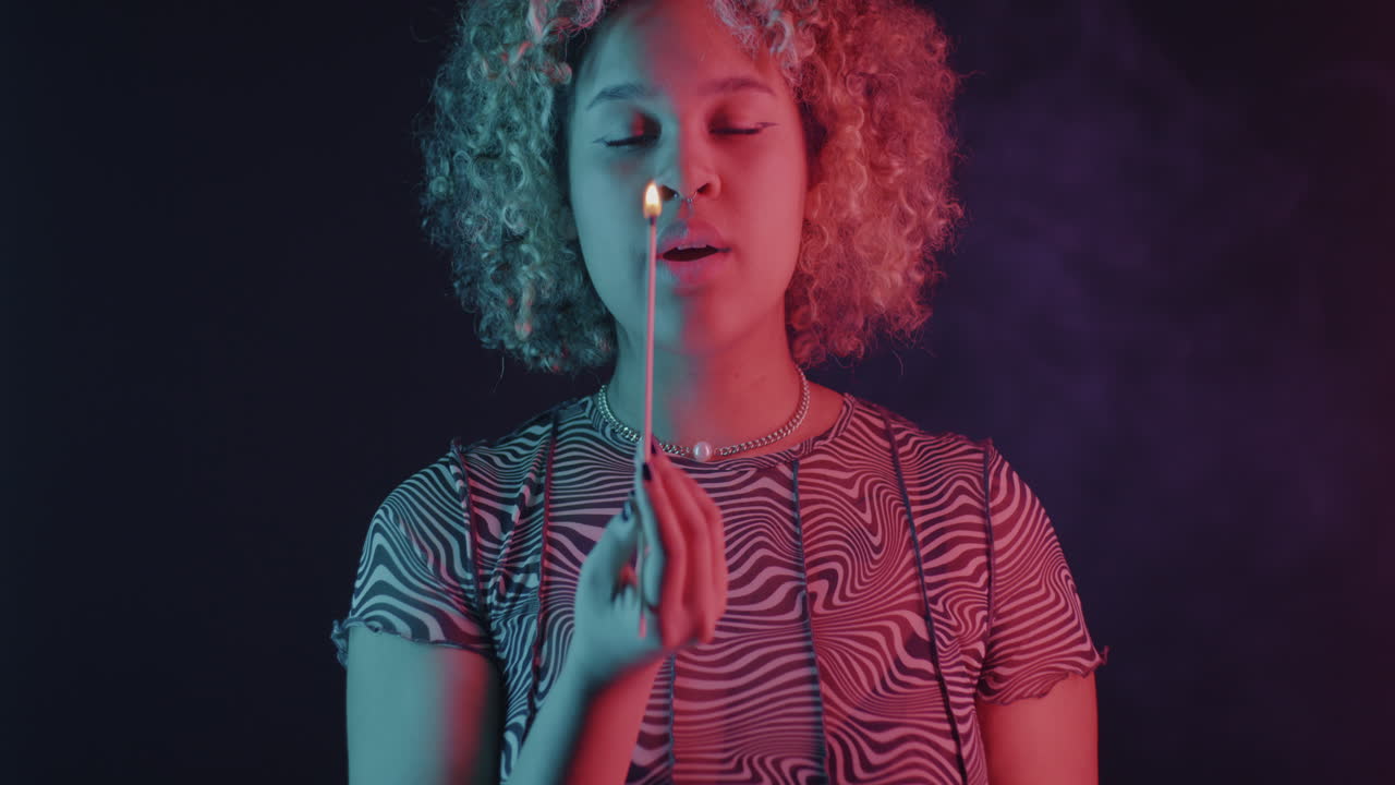 Woman with Curly Hair Holding a Match in Neon Lighting