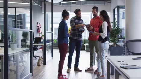 Diverse-group-of-work-colleagues-standing-looking-at-tablet-and-talking