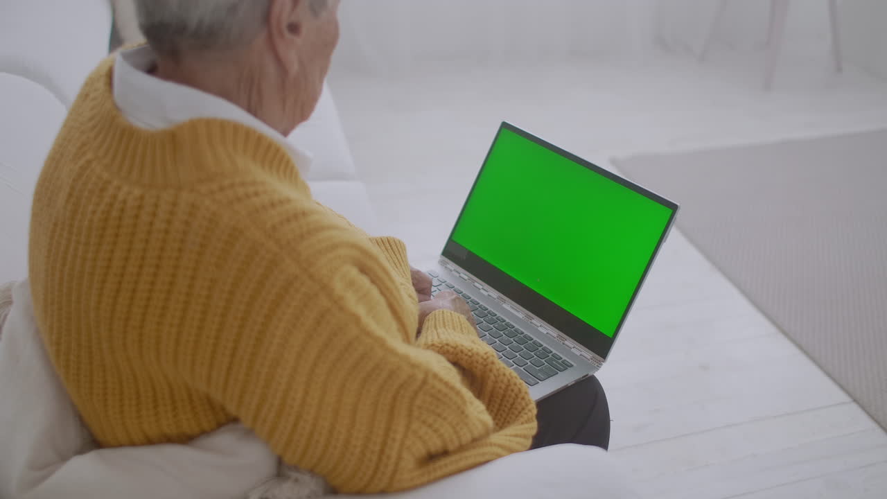 mujer madura asintiendo con la cabeza sí mientras mira una computadora de pantalla verde. mujer madura anciana con cabello gris y una videollamada en su computadora portátil. computadora portátil con pantalla verde
