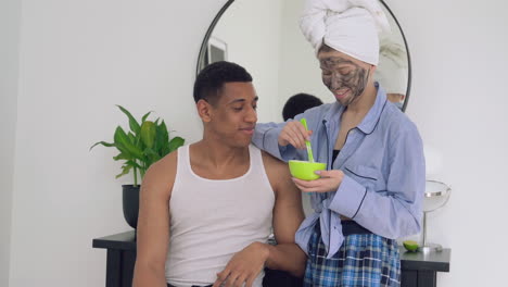 woman applying facial mask to a handsome black man