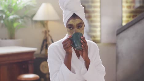 eafrican american attractive woman with applied face mask drinking coffee and using laptop at home