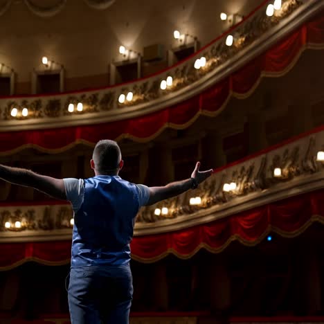 actor bowing on theatrical stage. man is standing on the scene of the classical theater and acting his role during the rehearsal before the empty hall. back view