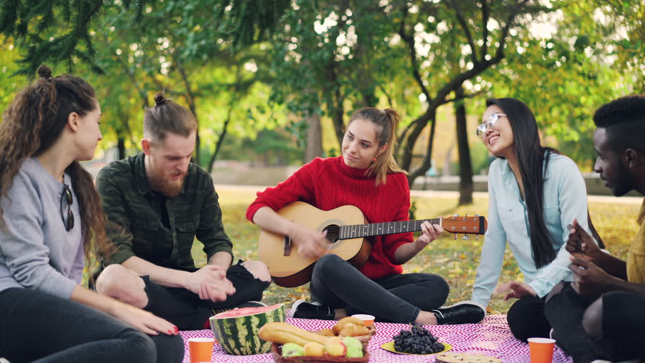 Friends enjoying a picnic in a park, playing guitar
