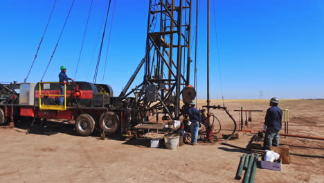 workers in protective helmets stand at the truck with drilling derrick. staff working at the site producing oil in the desert.
