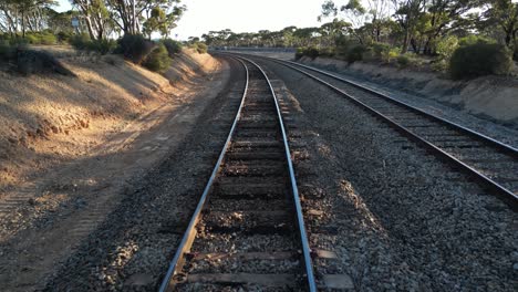 Drone-flying-at-low-altitude-over-train-rails-in-rural-landscape