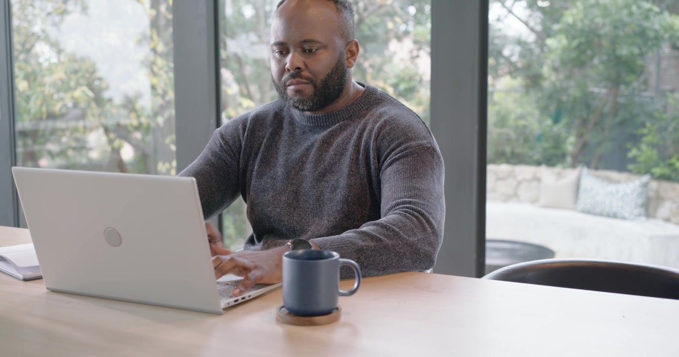 African couple woman rising from counter scrolling phone, revealing man typing for work on laptop
