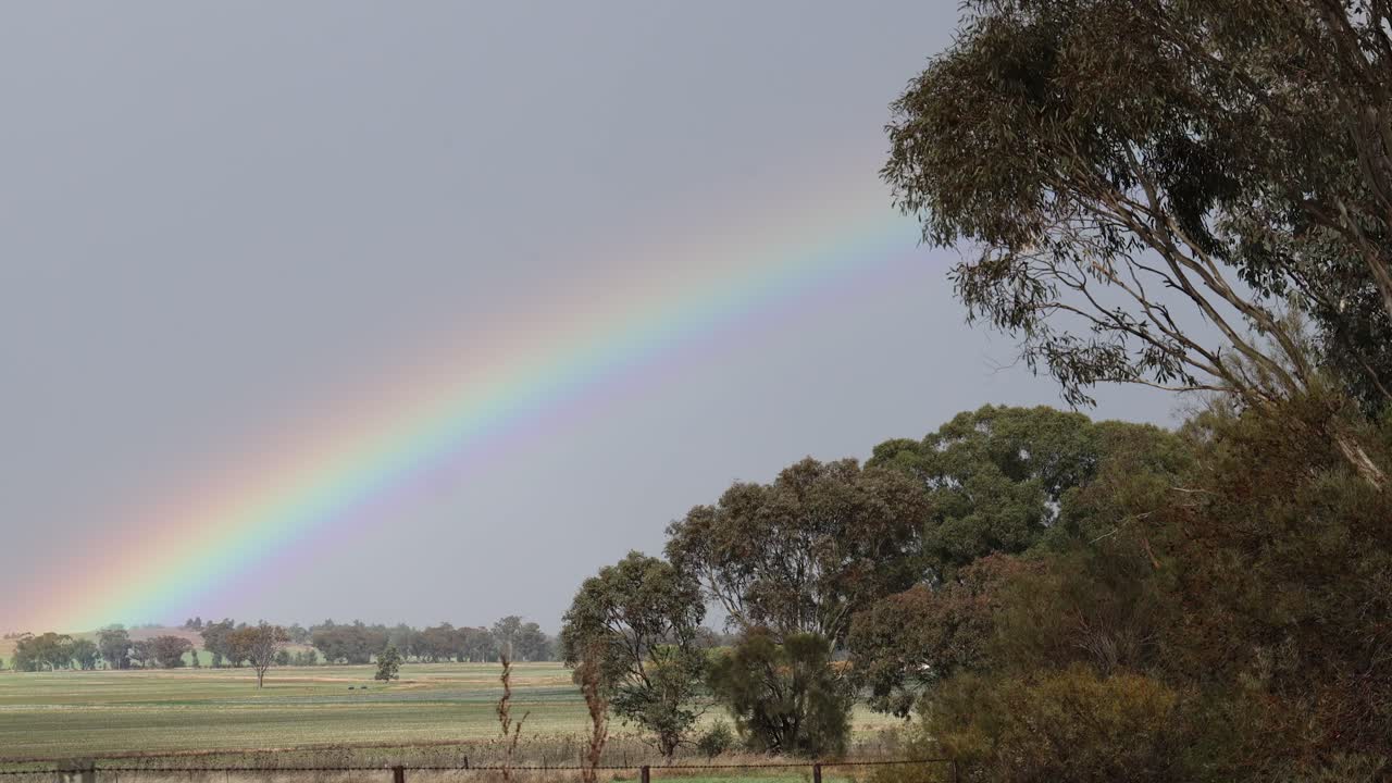 el lapso de tiempo de un arco iris que se desvanece sobre un campo