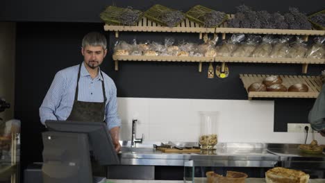 Handsome-father-in-apron-passes-a-tray-of-pastries-to-his-young-son-and-enters-data-into-the-bakery-database.-Indoor,-close-up