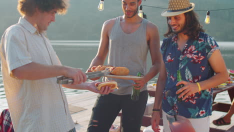 multiethnic male friends making hot dogs on lake party