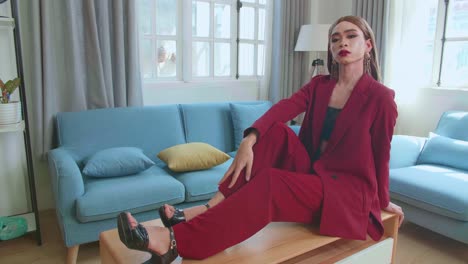 young fashion transgender woman wearing red clothes sitting on table and posing in home