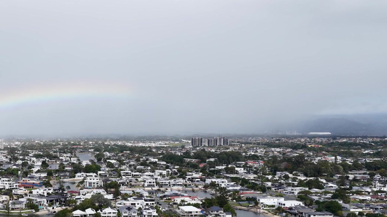 Ampia ripresa aerea di un arcobaleno che si estende su un quartiere residenziale costiero e corsi d'acqua.