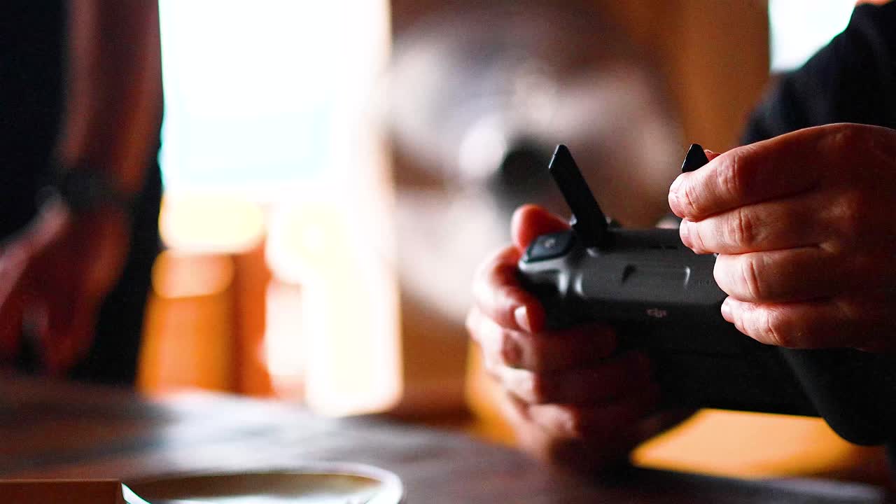 Hands operate a drone controller indoors with warm lighting, emphasizing focus and precision in a relaxed setting