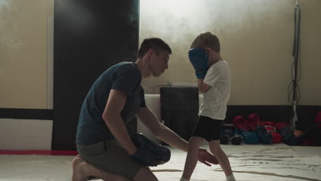 instructor shows leg position to child in sports gym. martial arts trainer teaches little boy boxing fight in club slow motion. children development