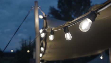 Slow-orbiting-shot-of-fairy-light-bulbs-hanging-around-the-canopy-at-a-wedding