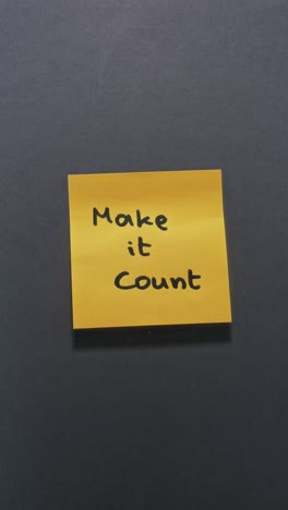 hands posting make it count sticky note on dark wall, demonstrating decisive action