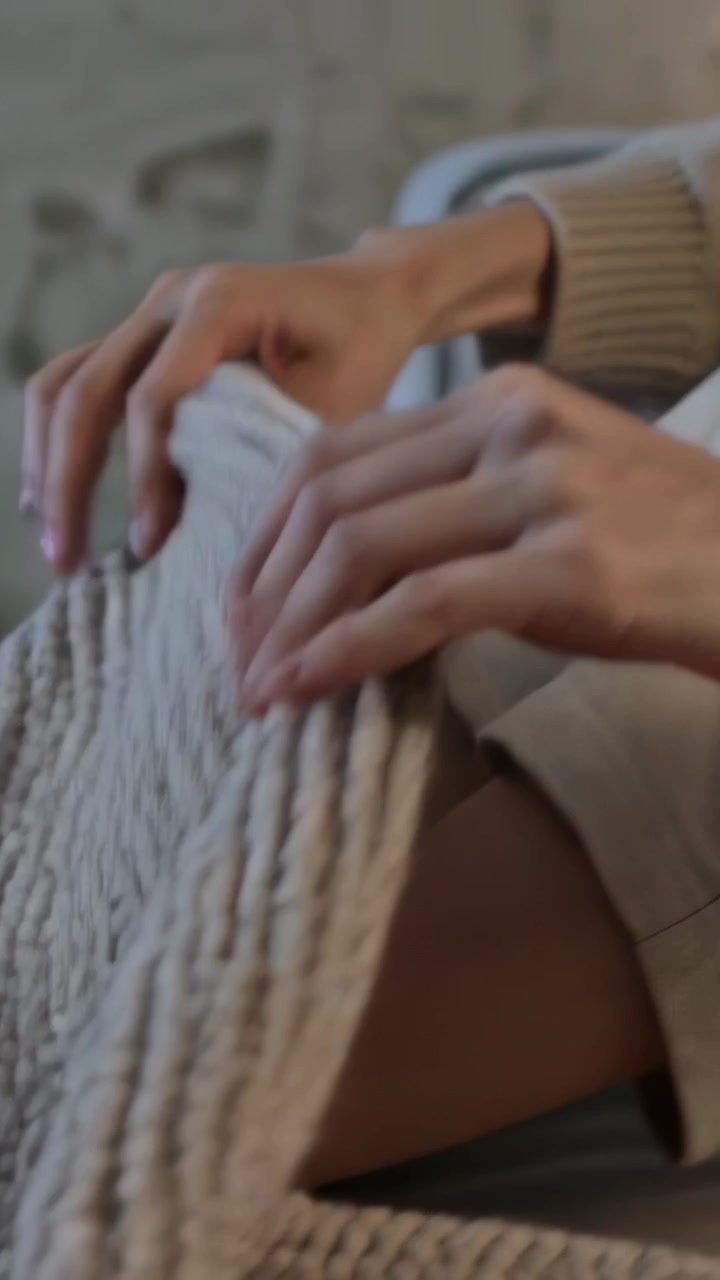 Video verticale: Mani con polsini a coste che liscia, solleva e piega una coperta sul letto per scaldarsi.