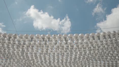 white color rounded pater lanterns with blessing cards hanging on lines for decoration against blue sky in buddhist temple on sunny day