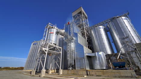 modern plant for agribusiness. silver grain elevators on blue sky background. granary on field. industrial factory with large storage bins at sunlight.