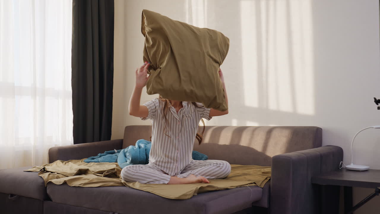 Youthful Playful Moment, Energetic Woman With Pillow, Vibrant Young Woman Tosses Pillow Inside Cozy Room, Lively Woman In Striped Pajamas Enthusiastically Throws Pillow In Intimate Living Area