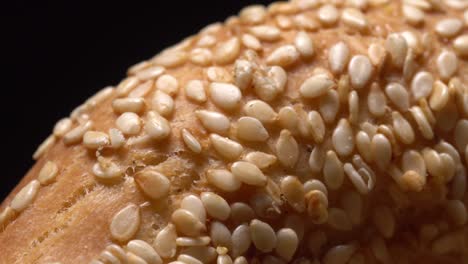 fresh bagels with sesame seeds in rotation. black background. extreme closeup.