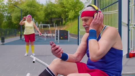 älterer mann hört nach dem sporttraining musik vom handy und trägt kopfhörer auf dem spielplatz