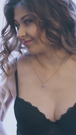 curly haired pregnant lady in elegant dark transparent bodysuit touches large tummy standing near window closeup