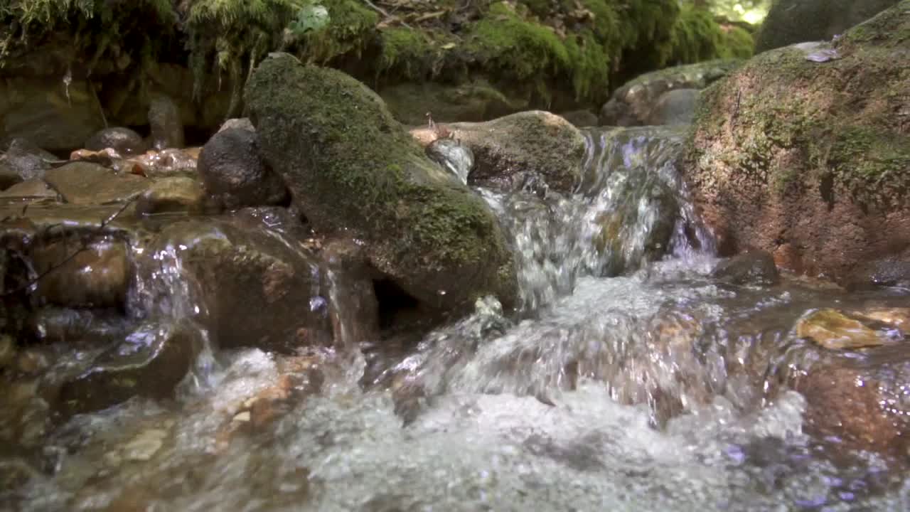 Running pure water of natural creek flowing down the mountain rocks