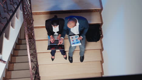 Top-view-of-overworked-coworkers-using-laptop-sitting-on-stairs