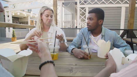 mujer joven hablando con sus amigos, mientras se sienta alrededor de una mesa al aire libre y come comida callejera