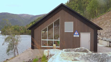 Powerplant-building-containing-four-megawatt-pelton-turbine-at-Markaani-powerplant-in-Vaksdal-Norway---Camera-moving-sideways-with-a-rock-in-blurres-foreground