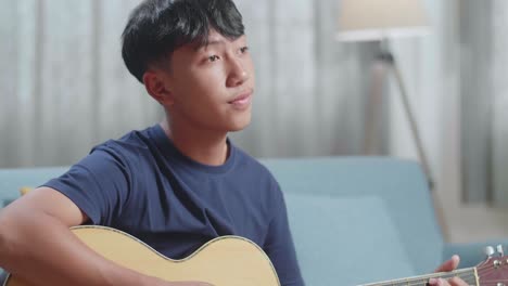 primer plano de un compositor asiático con un cuaderno en la mesa tocando la guitarra en casa