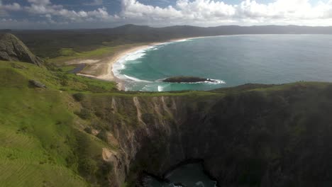 Beautiful-aerial-pull-back-reveal-rocky-cliffs-and-Spirits-Bay-in-Northland