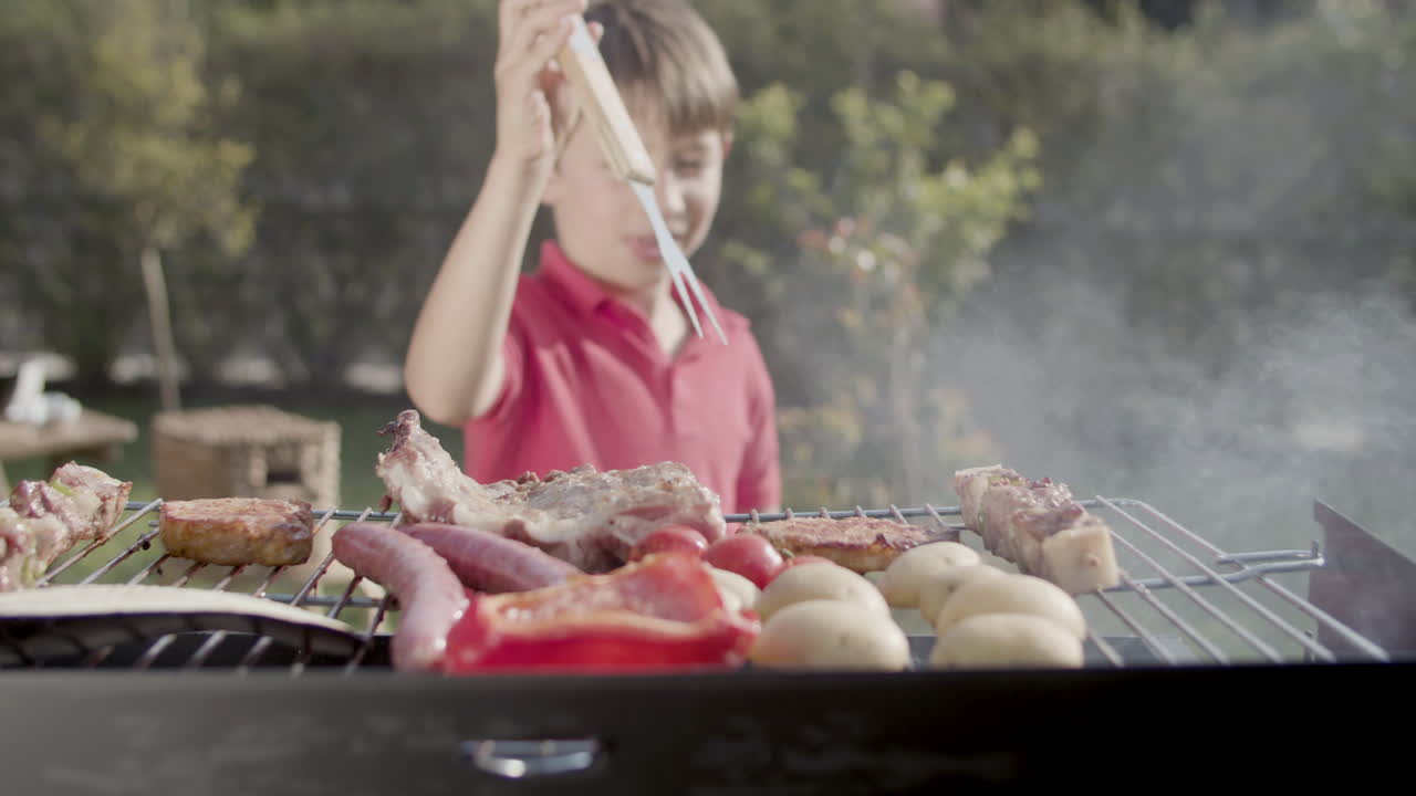 Ragazzo preadolescente felice che prende la carne con la forchetta dalla griglia per mangiarla