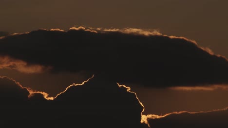 Red-and-orange-sunset-behind-dark-clouds,-static-wide-shot